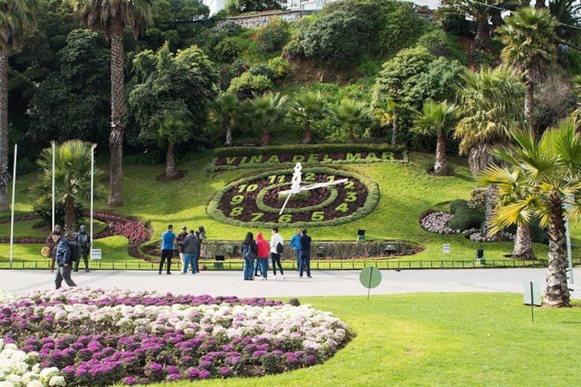 A park with a large clock garden, people walking, and a hill with greenery. 3