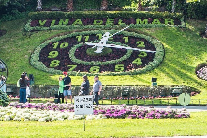 A garden with a large clock made of plants, a sign that says 'NO INGRESS,' and people standing around. 5