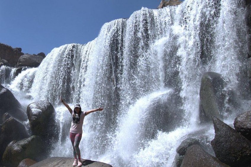A person standing on a rock with arms outstretched in front of a waterfall. 1
