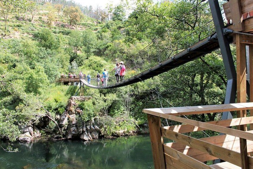 A wooden suspension bridge over a river, surrounded by lush greenery and rocky terrain. 4