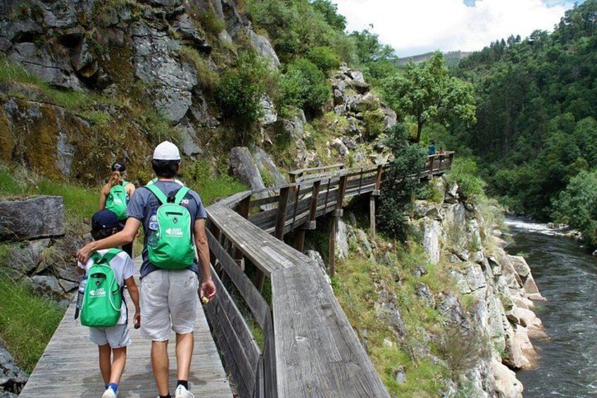 A wooden bridge over a river, surrounded by greenery and rocky terrain. 2