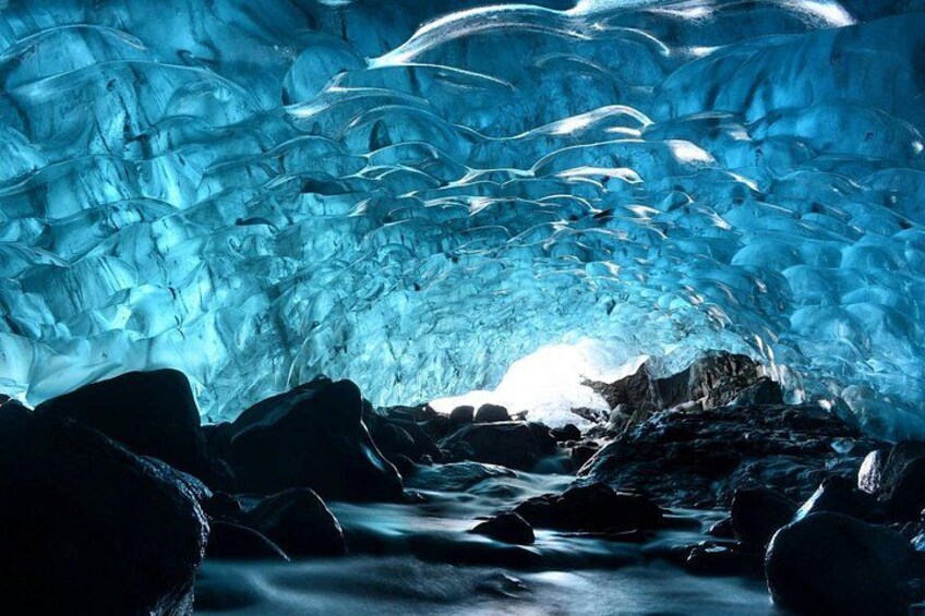 An ice cave with visible ice formations and a stream. 1