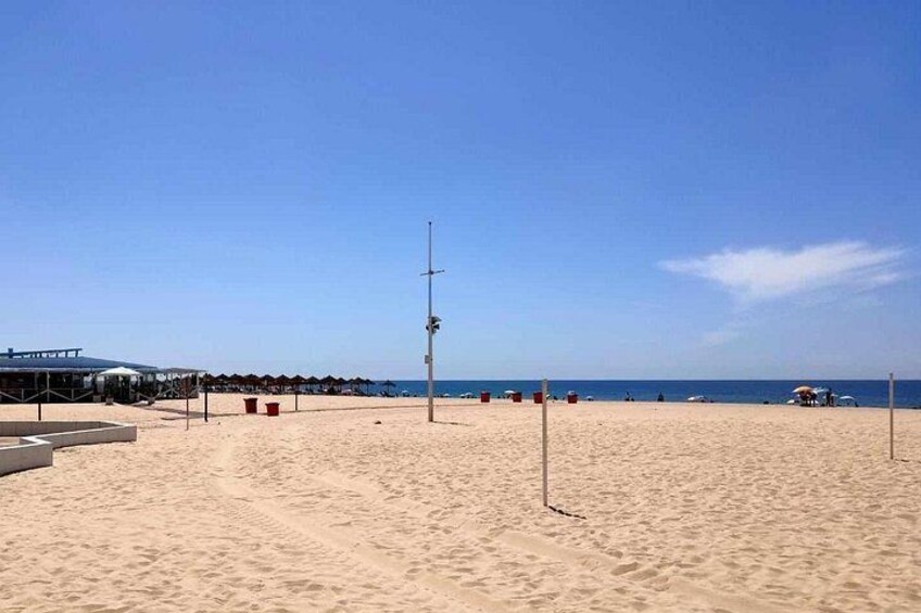 Une plage de sable avec un filet de volley-ball, des parasols et une tour de surveillance pour les sauveteurs. 3