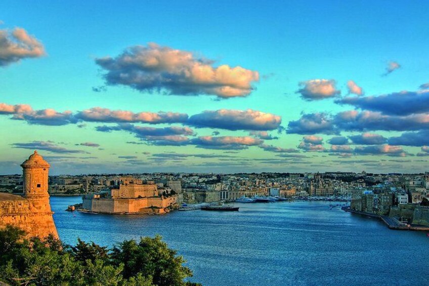 A coastal cityscape with a prominent tower, a fortified wall, and a calm sea. 2
