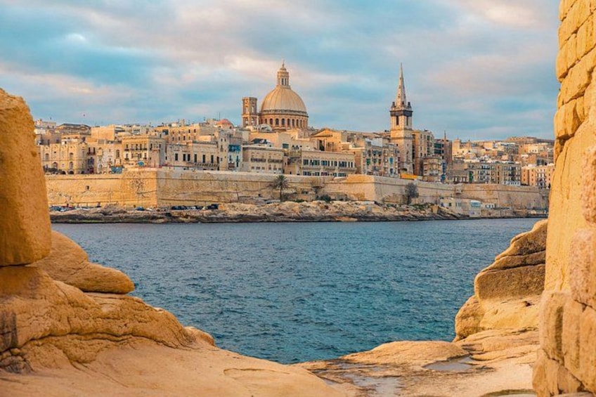 A coastal cityscape with prominent buildings, including a dome and a spire, and rocky cliffs in the foreground. 4