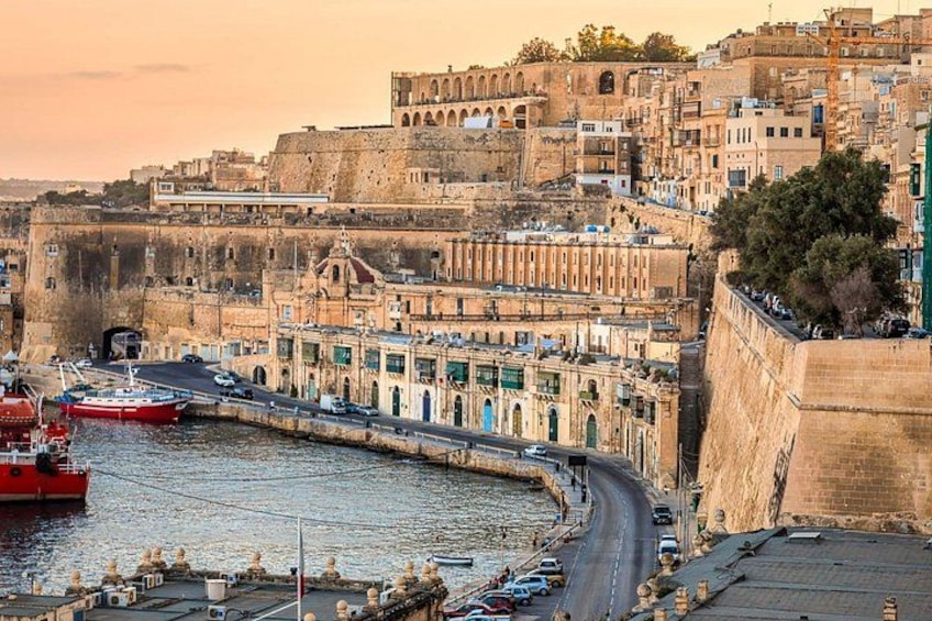 A coastal cityscape with historic buildings, a harbor with boats, and a prominent fortification. 2