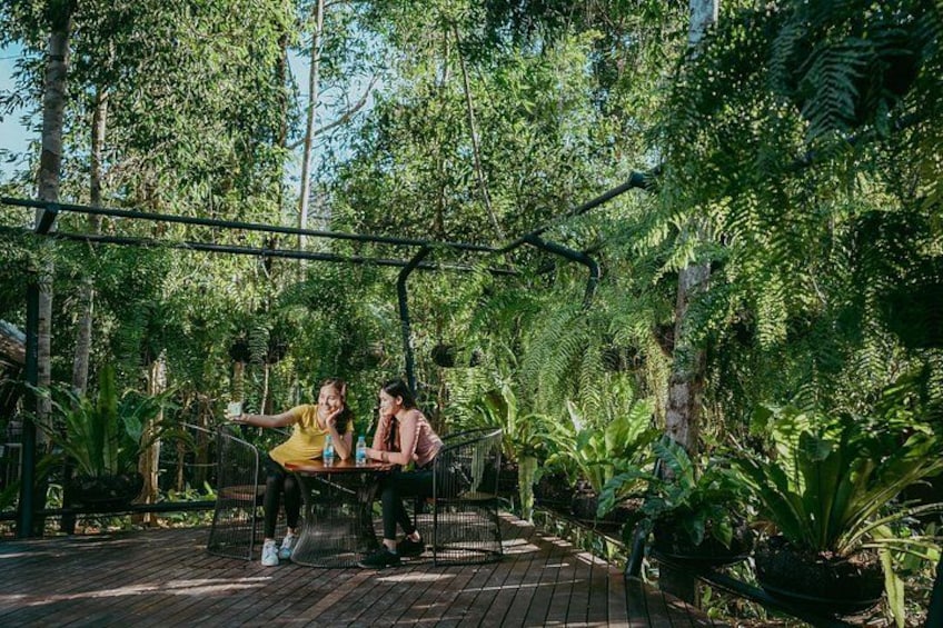 Dos personas en una terraza de madera rodeada de exuberante vegetación y árboles. 3