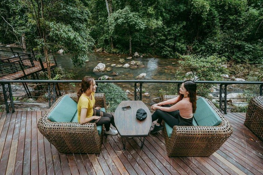Dos personas sentadas en muebles de mimbre en una terraza de madera con vista al río. 4