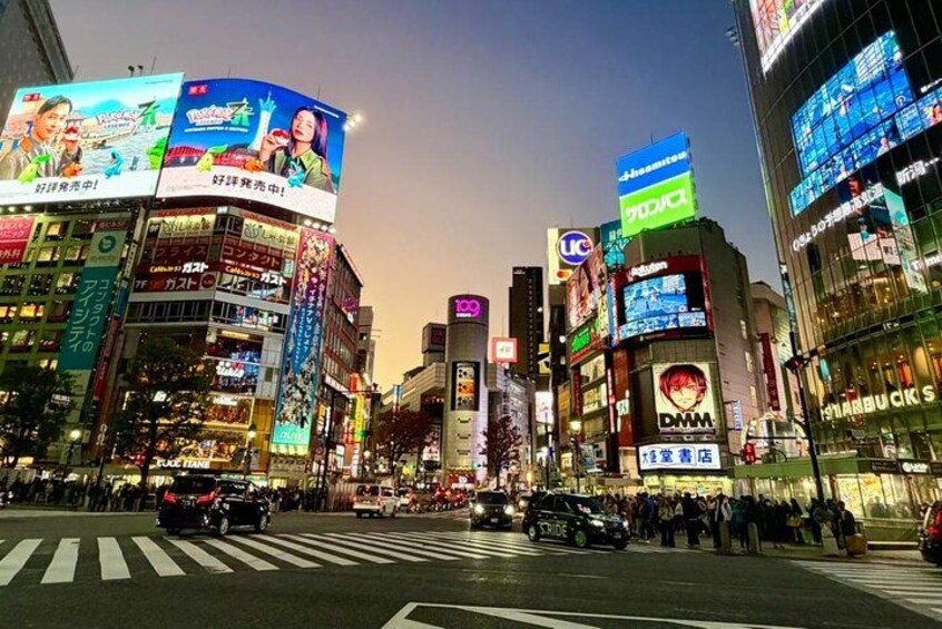 A busy urban street at dusk with illuminated billboards and storefronts. 3