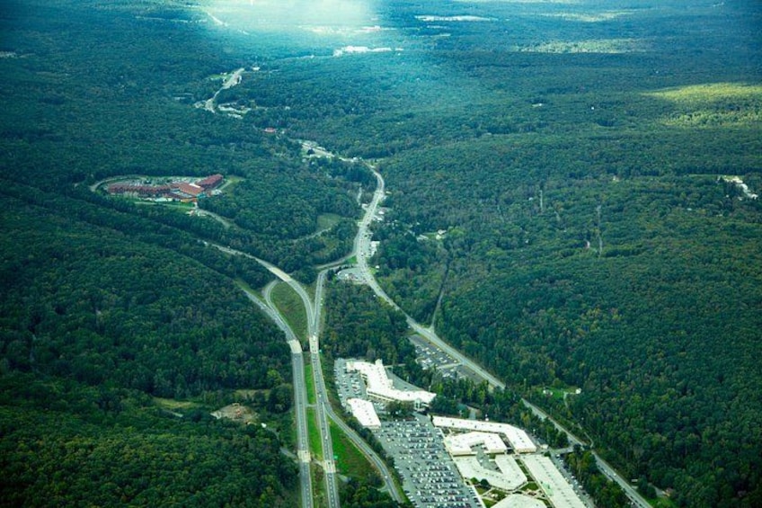 Vista aérea de una zona boscosa con una carretera serpenteante, un complejo de edificios grande y una pequeña estructura roja. 3