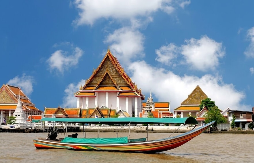A traditional boat with a colorful design on water, a temple with a golden roof, and a clear blue sky. 2