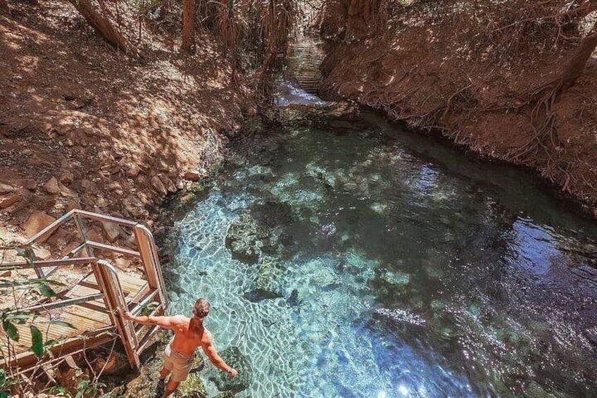 A person standing on a wooden staircase overlooking a clear, rocky stream. 1