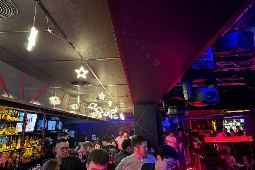 A crowded bar with neon lights and star-shaped decorations. 2