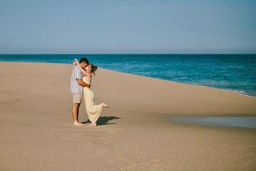 A couple embracing on a sandy beach with the ocean in the background. 3