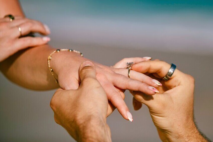 Two hands exchanging rings, one with a bracelet, against a blurred background. 4