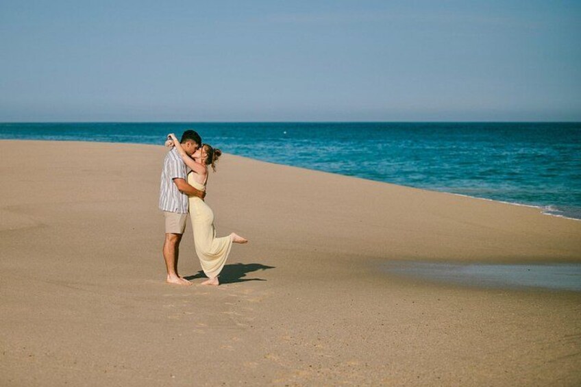 A couple embracing on a sandy beach with the ocean in the background. 2