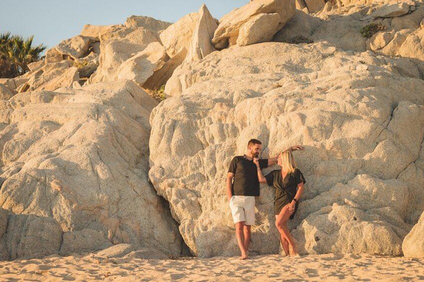 A couple standing on a sandy beach with large rock formations in the background. 3