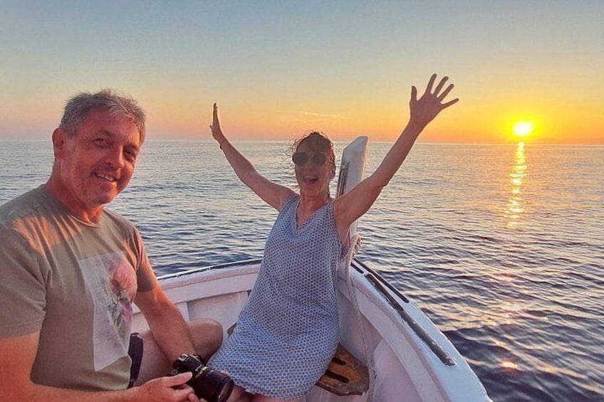 A boat on calm waters during sunset with a person raising their arms in celebration. 1