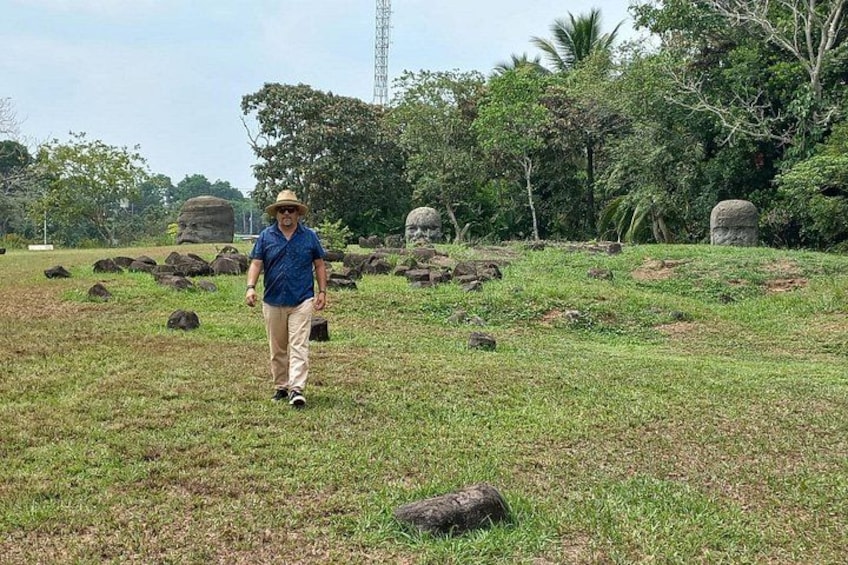 Eine Person geht durch eine grasbewachsene Landschaft mit großen Felsen und Bäumen im Hintergrund. 3