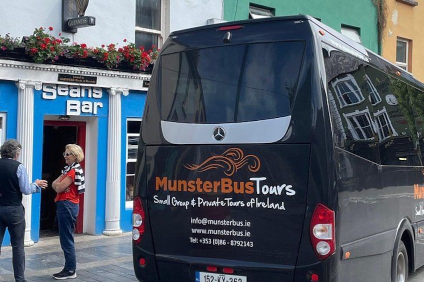 A black bus with MunsterBusTours branding parked in front of a bar. 2