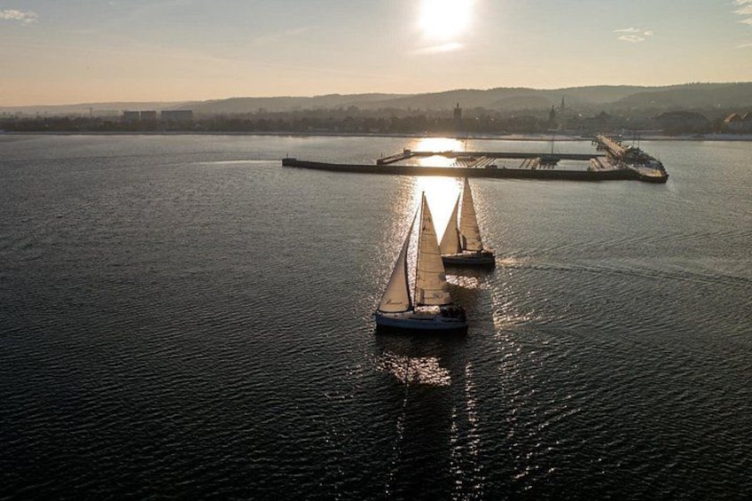En stilla flod med två segelbåtar, en brygga och en avlägsen stadsbild i bakgrunden. 1