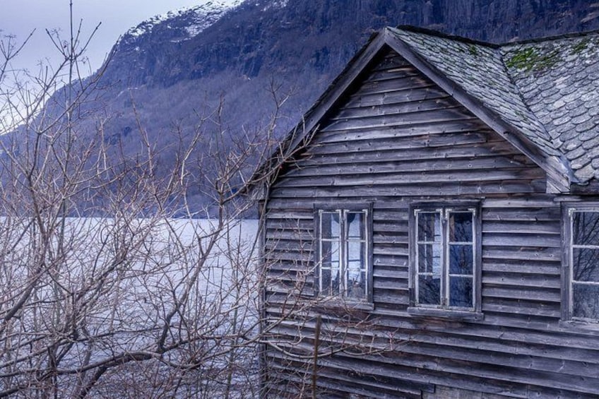 A wooden cabin with a steep roof, surrounded by bare trees and a mountainous backdrop. 3