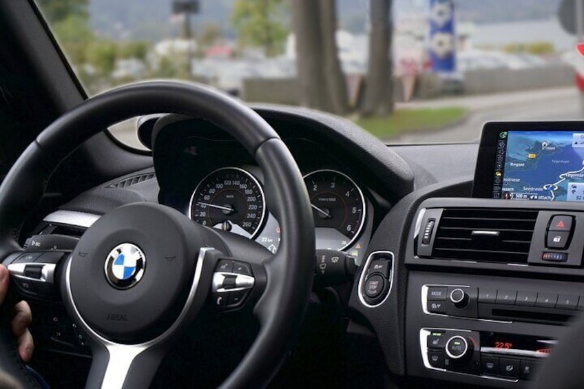 A BMW car interior with a steering wheel, dashboard, speedometer, and infotainment system. 5
