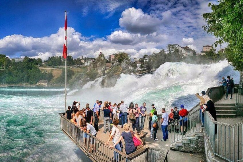 A crowd watching a waterfall, a flag, and a rocky landscape. 1
