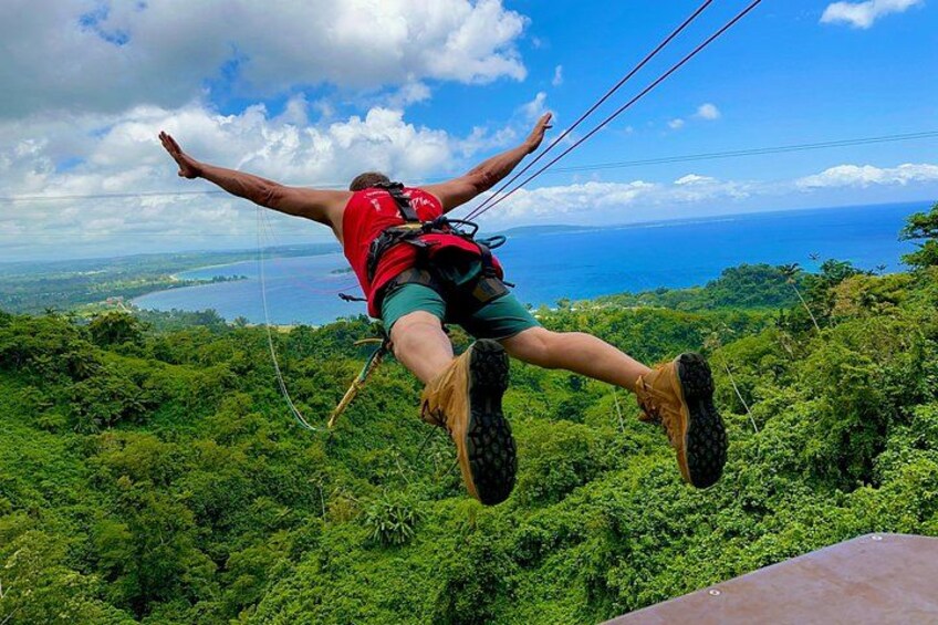 Eine Person macht Bungeesprung mit einem Gurt, umgeben von üppigem Grünland und Blick auf den Ozean. 3