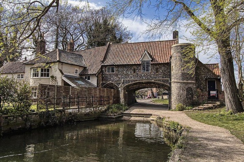 A stone bridge over a canal, surrounded by trees and a traditional house with a tiled roof. 3
