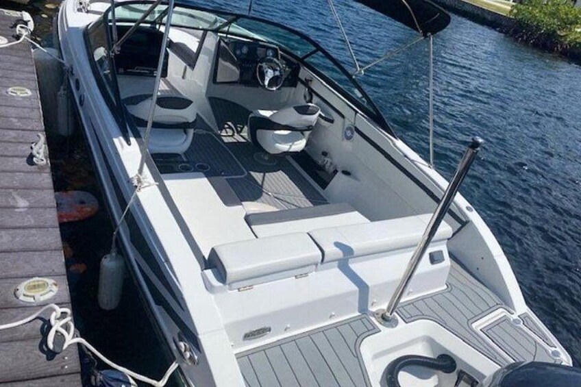 A boat docked at a pier with a wooden deck, a steering wheel, and a seating area. 1