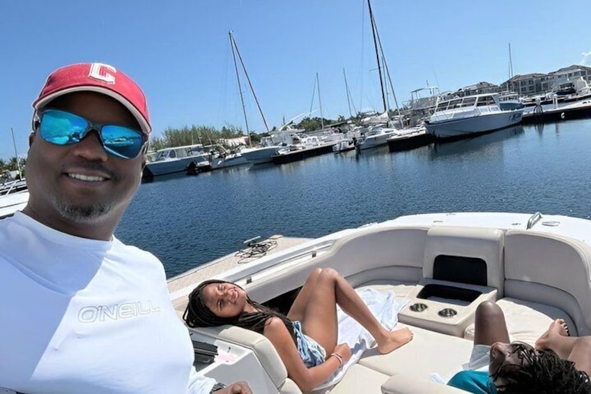 A boat with people relaxing on deck, a marina with multiple boats, and a clear blue sky. 3