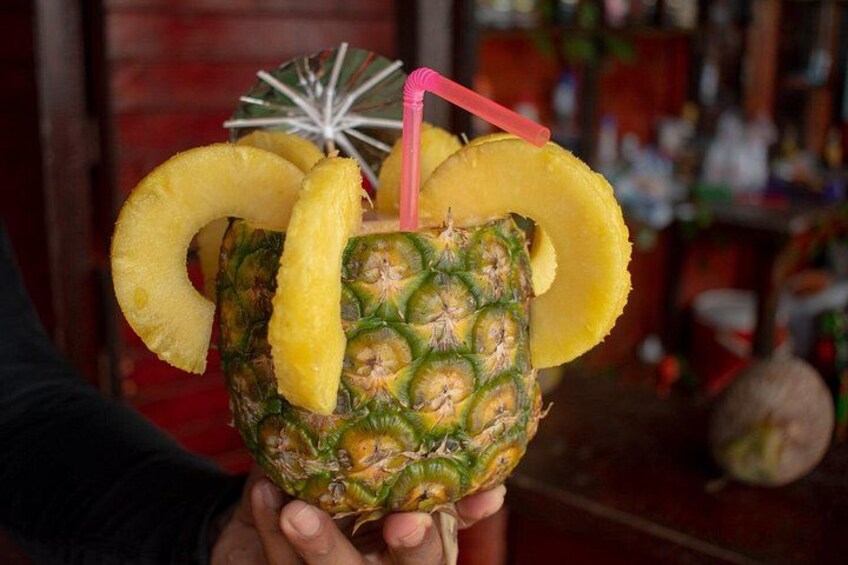 A person holding a pineapple with slices and a straw. 3