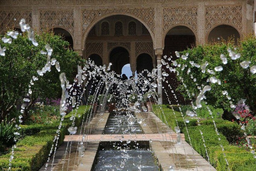 A water fountain with multiple streams, surrounded by lush greenery and ornate architecture. 5