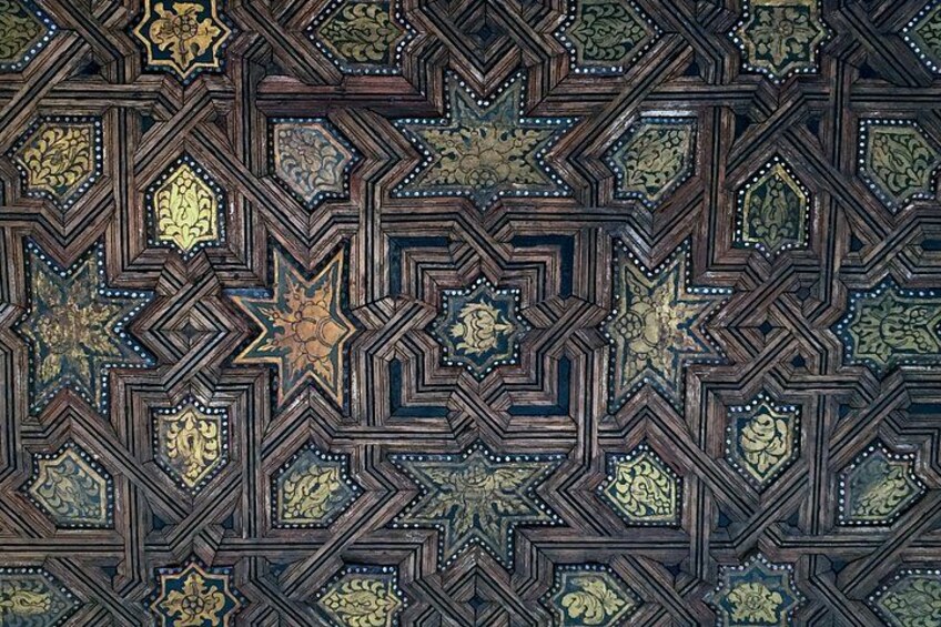 A detailed geometric pattern on a wooden ceiling with star and diamond shapes, adorned with gold accents and floral motifs. 2