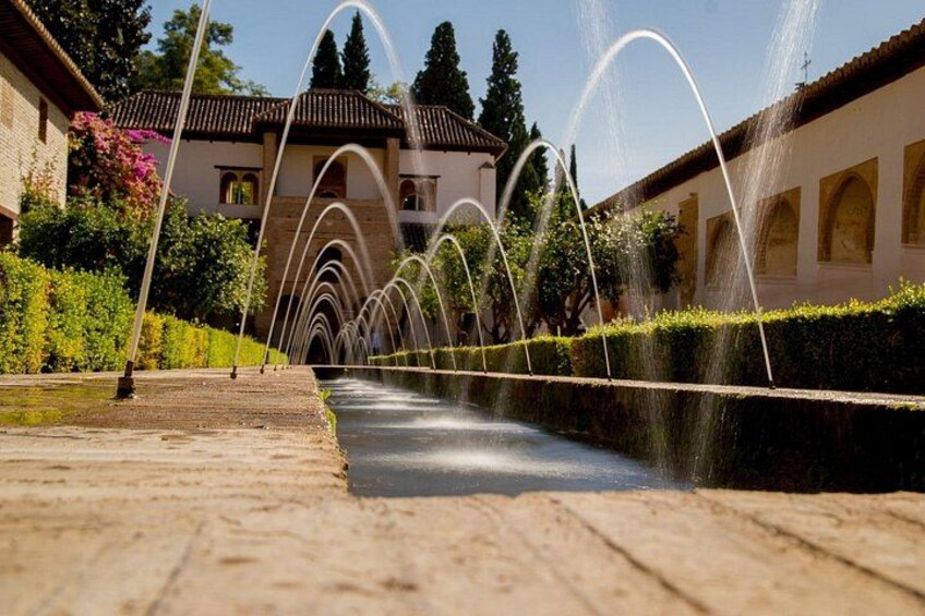 A fountain with water arcs in a courtyard with a building in the background. 1