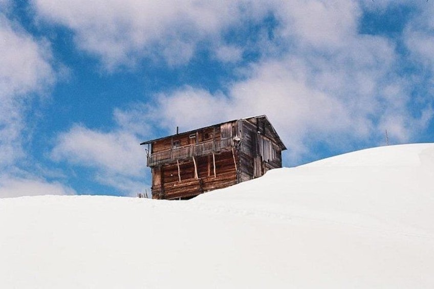 Eine Holzhütte auf einem mit Schnee bedeckten Hügel unter blauem Himmel mit Wolken. 2