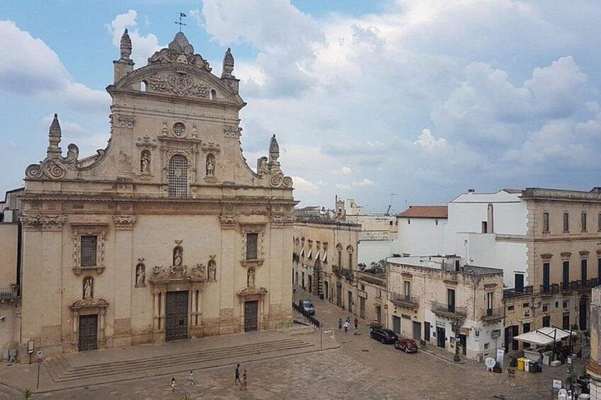 A historic church with ornate architecture, a cobblestone plaza, and surrounding buildings. 4