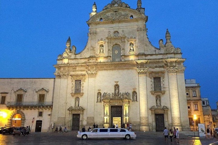 A historic cathedral with ornate architecture, a white car parked in front, and people walking around. 3