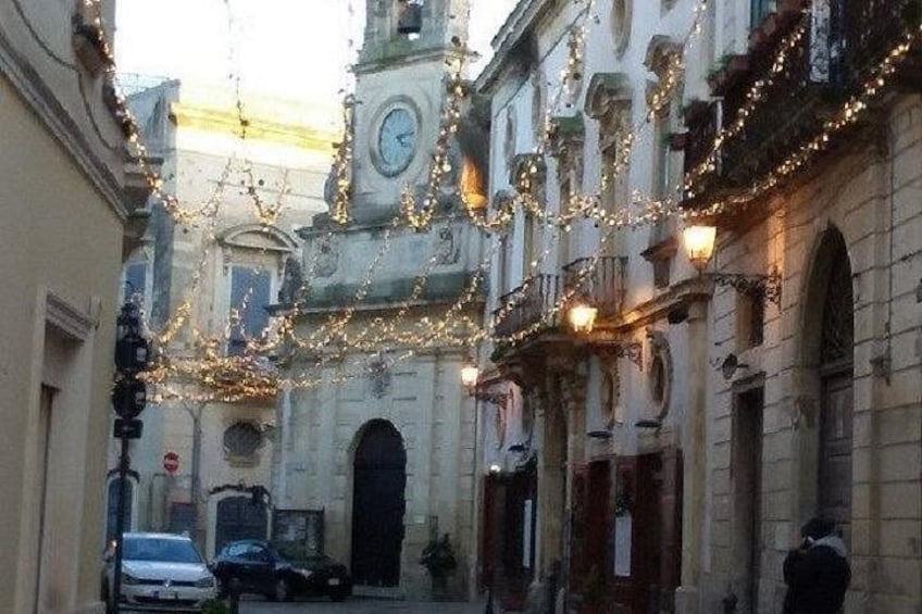 A narrow street with buildings, a clock tower, and string lights. 5