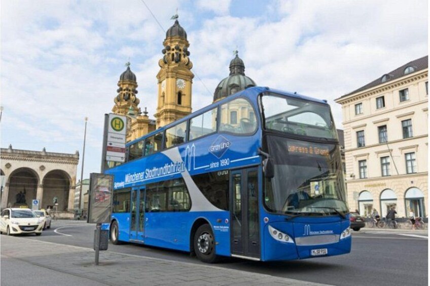 Un autobus à deux étages bleu, portant l’inscription « München Stadtbahn », est garé devant un bâtiment historique doté de deux tours. 4