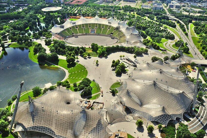 Vue aérienne d’un complexe architectural moderne comprenant un stade central, des espaces verts environnants et une étendue d’eau. 2