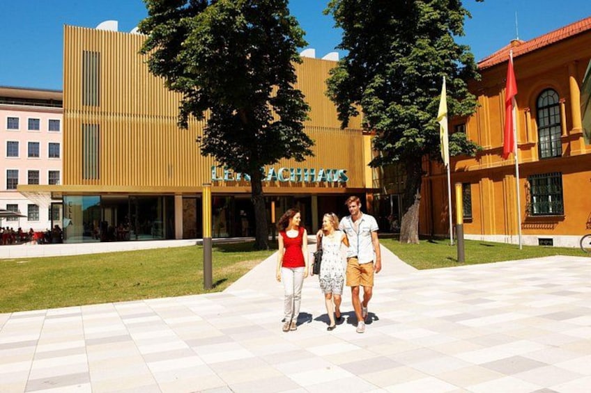 Un groupe de personnes se promène sur une zone pavée, et on aperçoit en arrière-plan un bâtiment sur lequel on peut lire l'inscription « LEONARDO ». 2