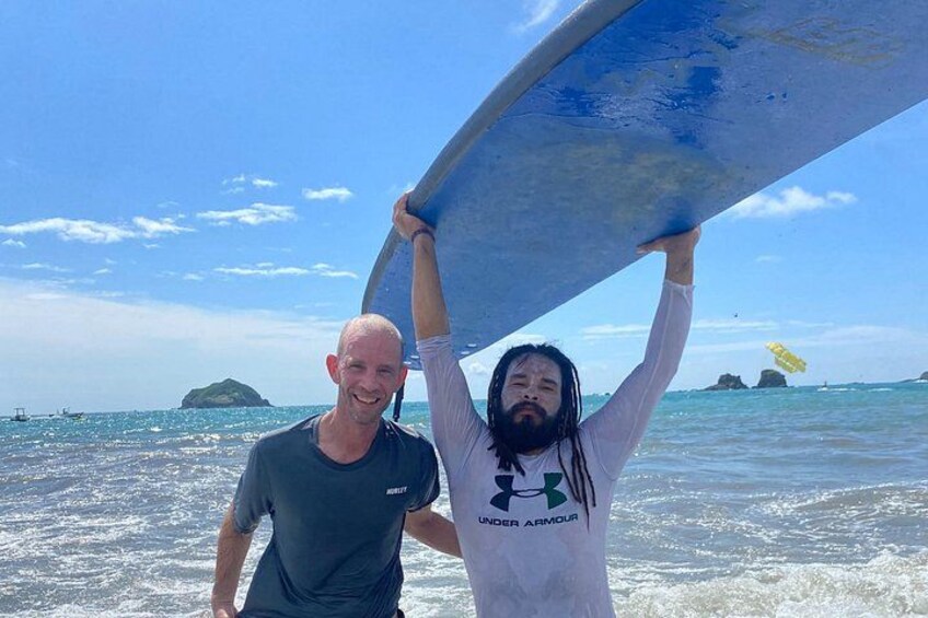 Two people holding a surfboard on a beach with clear skies and calm waters. 2