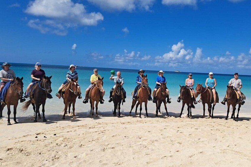 Un groupe de personnes à cheval sur une plage de sable, avec l’océan en arrière-plan. 5