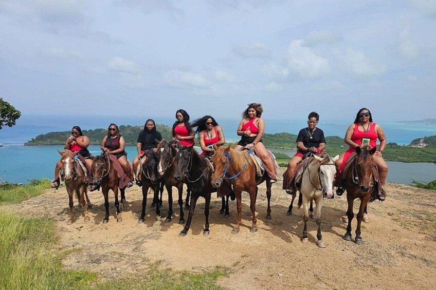 Un grupo de personas montando a caballo por un sendero de tierra, con un paisaje costero al fondo. 2
