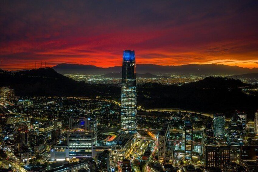 Paesaggio urbano al crepuscolo con un grattacielo in evidenza, edifici illuminati e montagne sullo sfondo. 2