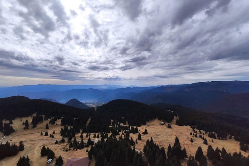 A mountainous landscape with a dirt path, scattered trees, and distant hills under a cloudy sky. 1