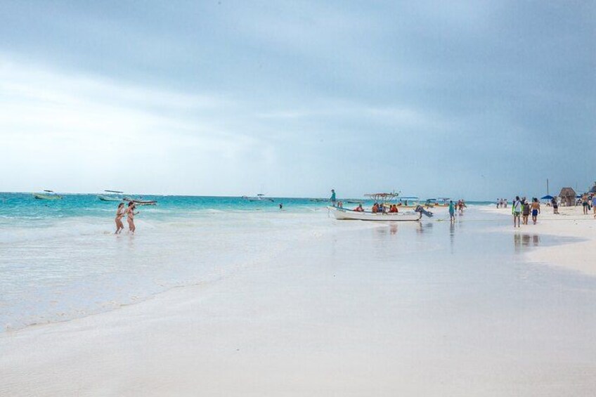 A beach with people walking, a boat, and a hut in the distance. 4