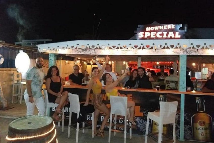 A bar with outdoor seating, a sign reading 'NOWHERE SPECIAL,' and a bottle of Bacardi 8 on the counter. 1